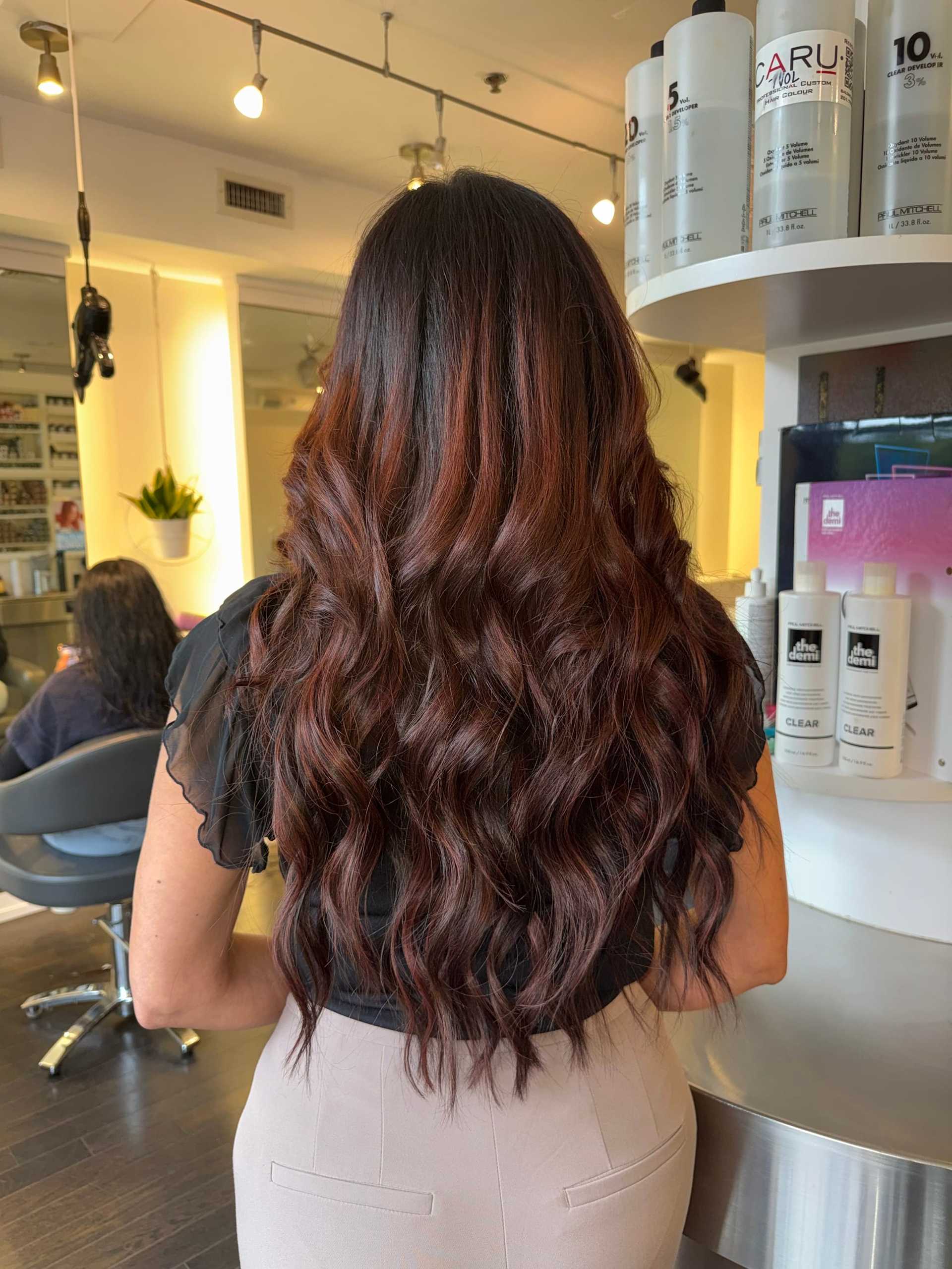 Long wavy brown hair in a salon, surrounded by hair products and stylist stations.