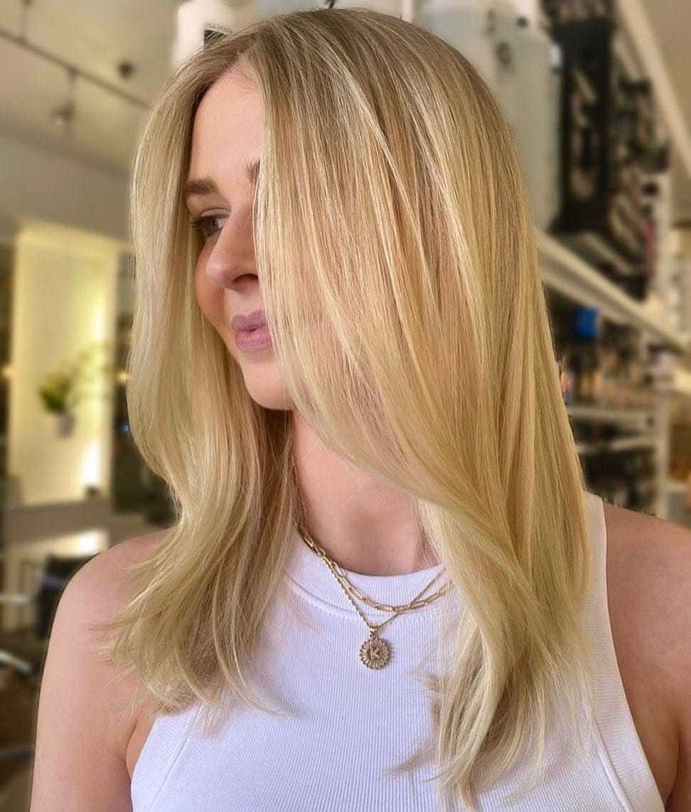 Blonde woman in white top with layered hair, smiling in a stylish salon.