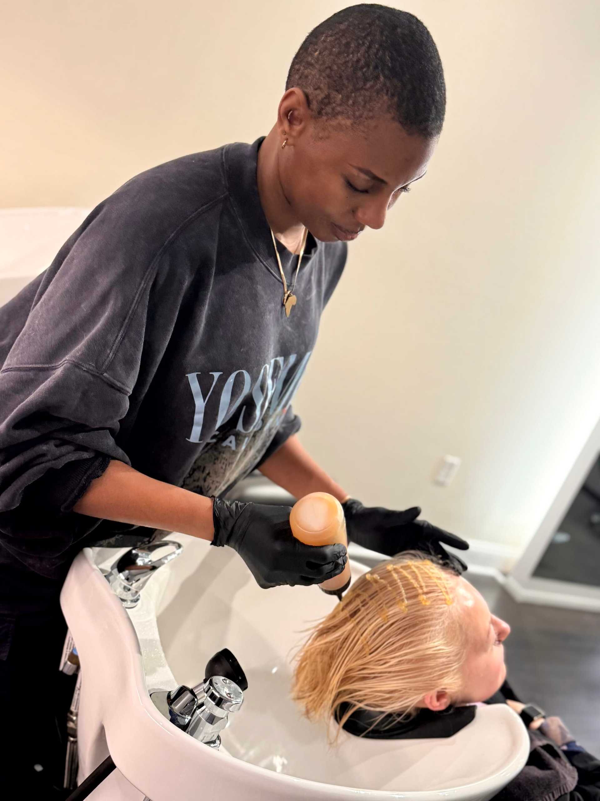 Hairstylist applying bleach to a client's hair at a salon sink.