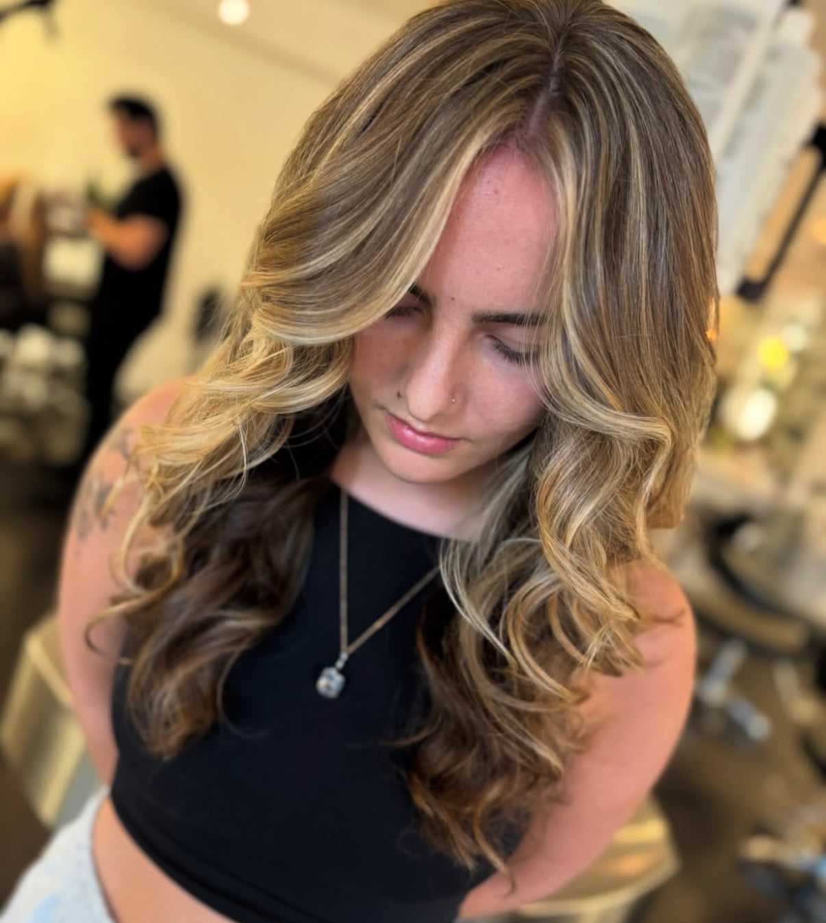 Woman with long, wavy blonde hair looking down in a salon setting.